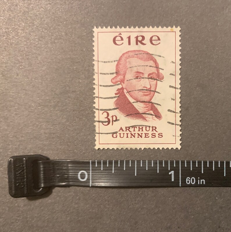May include: A vintage Irish postage stamp featuring a portrait of Arthur Guinness, the founder of the Guinness brewery. The stamp is red and white and has the text "&eacute;ire" and "3p ARTHUR GUINNESS" printed on it.
