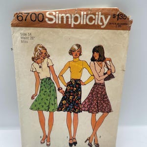 May include: Vintage Simplicity sewing pattern, style 6700, featuring illustrations of three women wearing wrap skirts. The pattern is size 14 with a 28-inch waist. The cover is tan with the Simplicity logo.