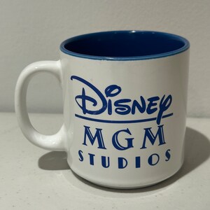 May include: White ceramic mug with a blue interior and blue lettering that reads "Disney MGM Studios".