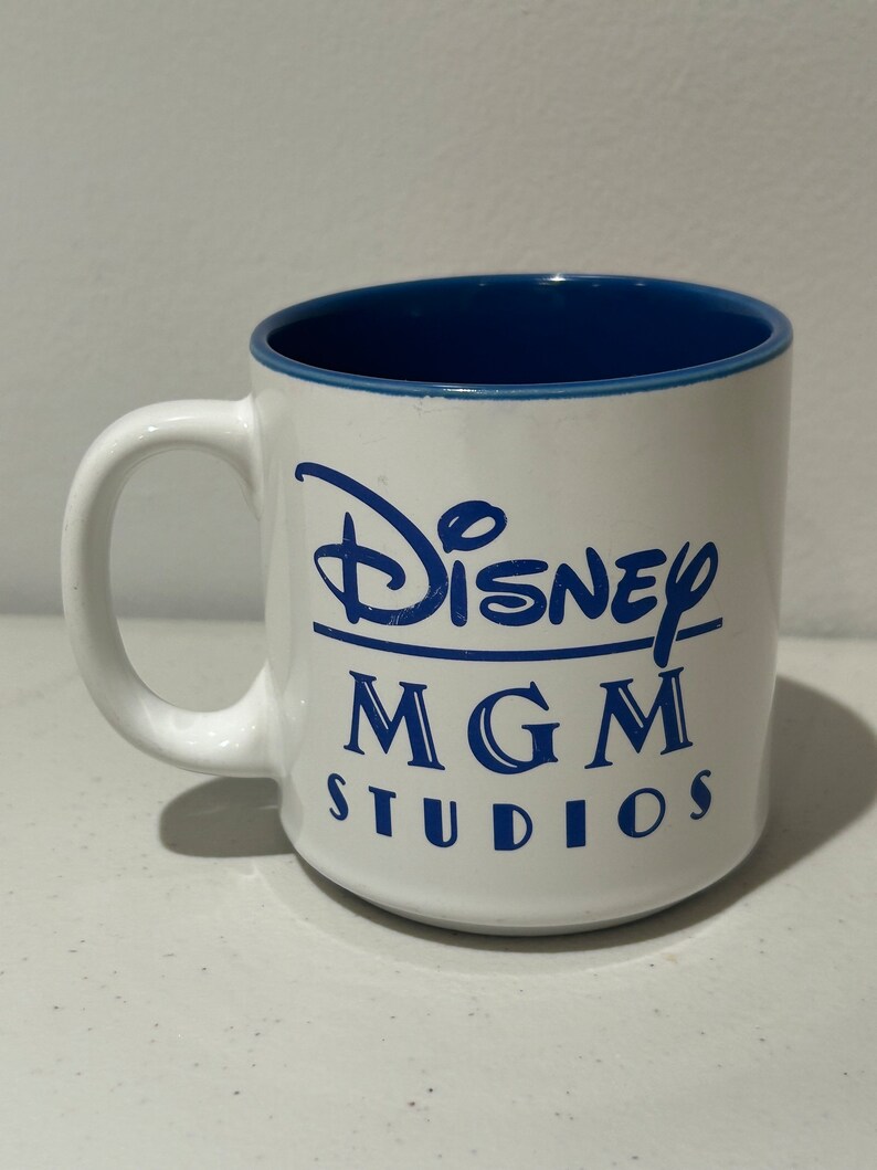 May include: White ceramic mug with a blue interior and blue lettering that reads "Disney MGM Studios".