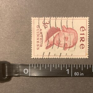 May include: A vintage Irish postage stamp featuring a portrait of Arthur Guinness, the founder of the Guinness brewery. The stamp is red and white and has the text "3p ARTHUR GUINNESS eIRE" printed on it.