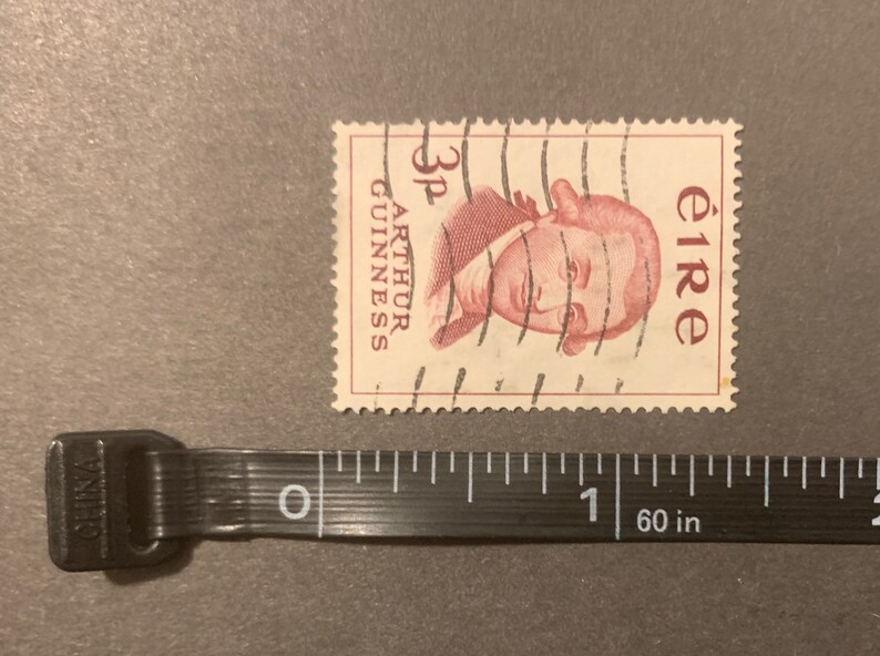 May include: A vintage Irish postage stamp featuring a portrait of Arthur Guinness, the founder of the Guinness brewery. The stamp is red and white and has the text "3p ARTHUR GUINNESS eIRE" printed on it.