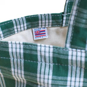 Op de afbeelding: Detail van een groen-witte geruite draagtas. De tas heeft een label met "MADE IN HAWAII" en een Hawaiiaanse vlag. De binnenkant van de tas is lichtbeige.