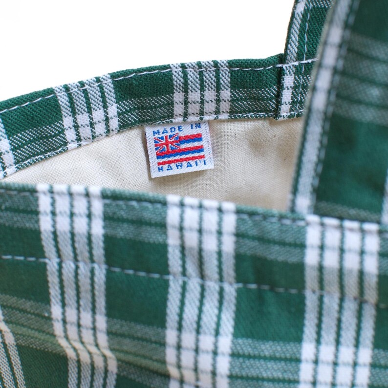 Op de afbeelding: Detail van een groen-witte geruite draagtas. De tas heeft een label met "MADE IN HAWAII" en een Hawaiiaanse vlag. De binnenkant van de tas is lichtbeige.