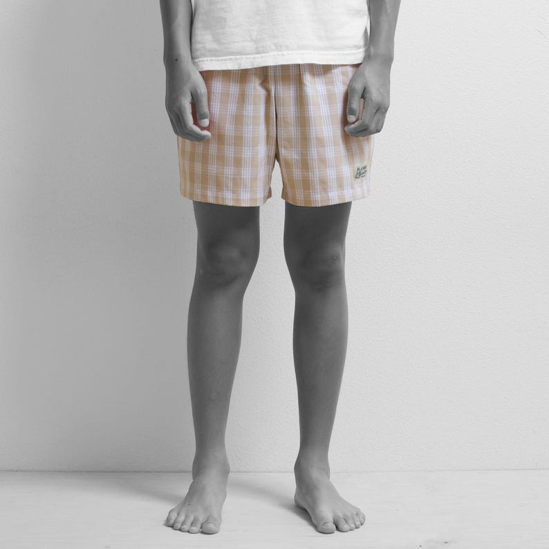 May include: A person wearing beige and white checkered shorts with a small green logo on the right leg.