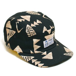 May include: A black five-panel cap with a beige geometric pattern. The cap features a flat brim and a small label with text and a palm tree graphic. The cap is made of a textured fabric.