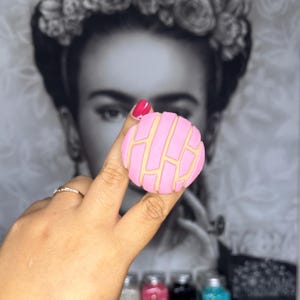 May include: A pink and beige concha, a traditional Mexican sweet bread, is held in a hand. The concha is a popular treat and is often enjoyed with coffee or tea.