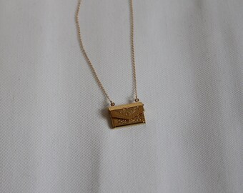 May include: A gold chain necklace with a small, ornate envelope pendant.
