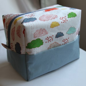 May include: A white zippered pouch with a blue base. The pouch has a colorful print of clouds and raindrops.