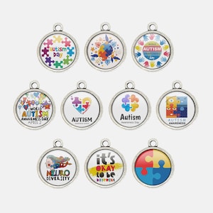 May include: A collection of silver-toned pendants with various designs related to autism awareness. The pendants feature colorful puzzle pieces, handprints, and text such as "Autism Day," "World Autism Awareness Day," and "Neuro Diversity."