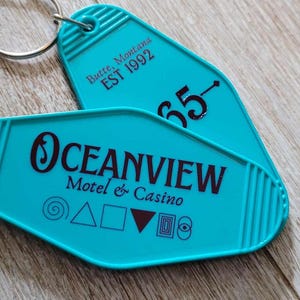 May include: Two turquoise motel keychains with key rings. The top keychain has the text "Batte Montana EST 1992" and the number "65". The bottom keychain has the text "OCEANVIEW Motel & Casino" and a series of symbols.