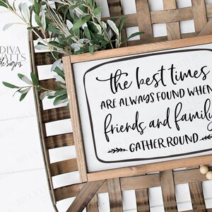 以下が含まれることがあります： 白い背景に黒い文字で「The best times are always found when friends and family gather round」と書かれた木製の看板。看板は、木製のビーズがついた籐のバスケットの上に置かれている。