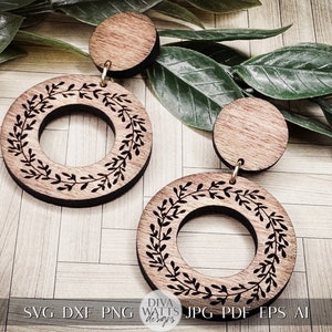 May include: A pair of wooden earrings with a circle design featuring a leafy wreath. The earrings are brown and have a gold-colored metal hook.