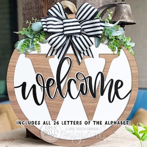 May include: A wooden welcome sign with a large white "W" and the word "welcome" in black script. The sign is decorated with greenery and a black and white striped bow. Includes all 26 letters of the alphabet.