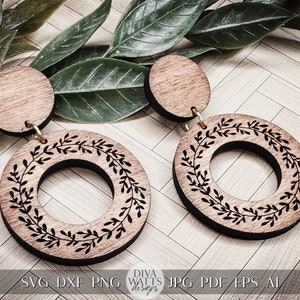 May include: A pair of wooden earrings with a circular design featuring a wreath of leaves. The earrings are brown with a natural wood finish and have a simple, elegant style.