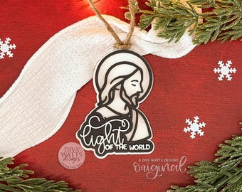 May include: A Christmas ornament featuring a black and white illustration of Jesus with the text "Light of the World." The ornament hangs from a twine string against a red background with snowflakes and greenery.