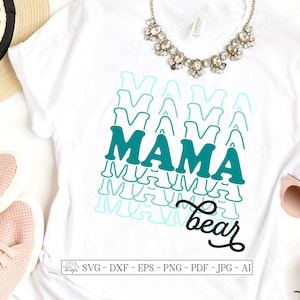 以下が含まれることがあります： 「MAMA」と黒色の筆記体で「bear」と書かれた、ターコイズブルーとライトブルーのグラフィックが施された白いTシャツ。グラフィックは、さまざまなサイズとブルーの濃淡で「MAMA」という単語が複数回重ねられたデザインです。