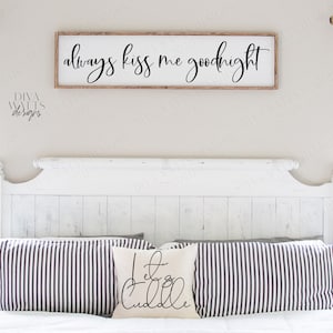 May include: A white bedroom with a white headboard and a sign above the bed that reads "always kiss me goodnight". There are two striped pillows on the bed and a pillow with the text "let's cuddle" on it.