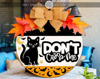 Könnte beinhalten: Runder Halloween-Holzschild mit einer schwarzen Katzenillustration und dem Text "DON'T CROSS ME". Das Schild hat orange, schwarze und weiße Farben, mit Herbstblättern und einer Schleife aus Jute.