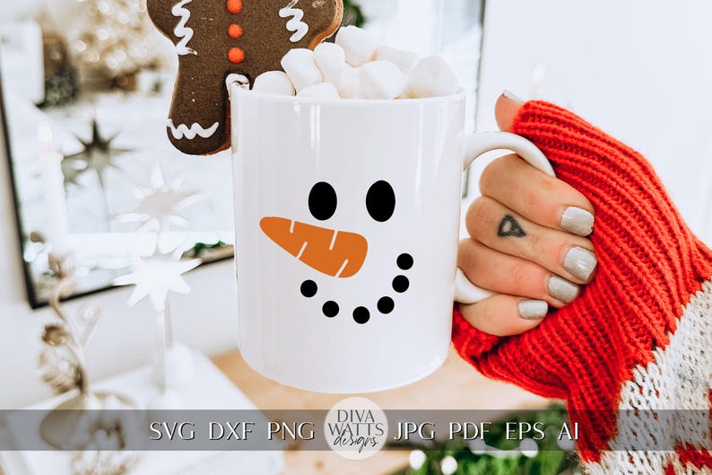 Peut inclure: Une tasse en c&eacute;ramique blanche avec un motif de visage de bonhomme de neige. Le bonhomme de neige a des yeux noirs, un nez de carotte orange et un sourire noir. La tasse est remplie de guimauves et d'un biscuit au pain d'&eacute;pices brun.