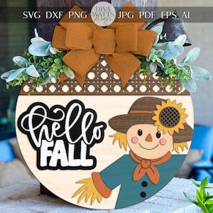 以下が含まれることがあります： 「Hello Fall」の文字とカカシが描かれた、秋をテーマにした丸い木製のドアハンガー。カカシは帽子にヒマワリをつけ、ティール色のシャツを着ています。上部には茶色のリボンと緑の葉が飾られています。
