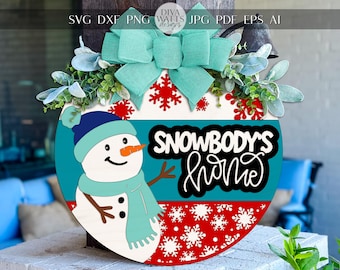 May include: A round wooden sign with a snowman design and the text "SNOWBODY'S home". The sign features a teal bow, snowflakes, and greenery. A cheerful winter-themed decoration.