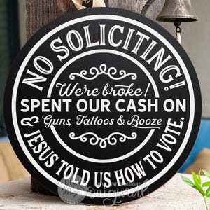 Könnte beinhalten: Runder, schwarzer Holzschild mit weißer Schrift. Auf dem Schild steht "NO SOLICITING!" und "JESUS TOLD US HOW TO VOTE." Es steht auch "We're broke! Spent our cash on Guns, Tattoos & Booze."