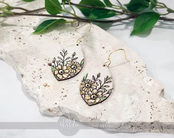May include: A pair of teardrop-shaped earrings with a floral design. The earrings feature a white background with a hand-painted design of yellow flowers and green leaves. The earrings have gold-colored ear wires.