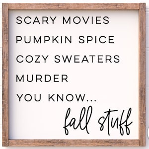 Op de afbeelding: Een wit houten bord met zwarte tekst die "Scary Movies, Pumpkin Spice, Cozy Sweaters, Murder, You Know... fall stuff" luidt. Het bord is omlijst met bruin hout.