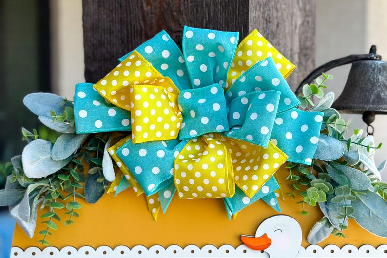 May include: A yellow and blue polka dot bow with a white background. The bow is made of ribbon and is tied in a knot. The bow is sitting on top of a yellow surface.