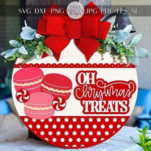 Puede incluir: Un letrero navide&ntilde;o redondo de madera con un lazo rojo, vegetaci&oacute;n y la frase "Oh Christmas Treats". El letrero presenta ilustraciones de macarons y bastones de caramelo, con un borde de lunares rojos y blancos.