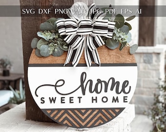 May include: A round wooden sign with a black and white striped bow, greenery, and the text "home sweet home" in black script. The sign has a black and white chevron pattern at the bottom.
