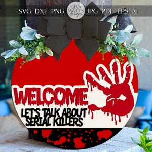 May include: A round, red and white wooden welcome sign with the text "WELCOME LET'S TALK ABOUT SERIAL KILLERS". The sign features a bloody handprint and is decorated with a black bow and greenery.