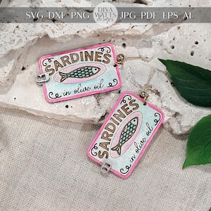 May include: A pair of wooden earrings with a retro sardine tin design. The earrings have a pink border, a light blue background, and the words "Sardines in olive oil" with a fish illustration. They hang from gold-coloured hooks.