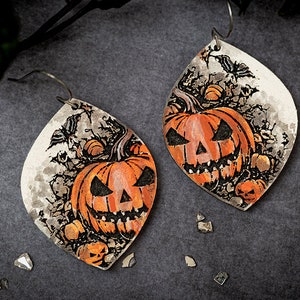 May include: A pair of Halloween-themed earrings featuring a jack-o'-lantern design on a white background with black vines and bats. The earrings are made of metal and have a silver finish.