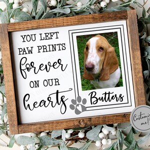 Może przedstawiać: Biały drewniany znak z brązową ramą, przedstawiający czarną łapę i tekst "You left paw prints forever on our hearts." Zdjęcie basset hounda znajduje się w ramce na znaku, z napisem "Butters" poniżej. Znak ma szare koło z tekstem "Customize me!" na nim.