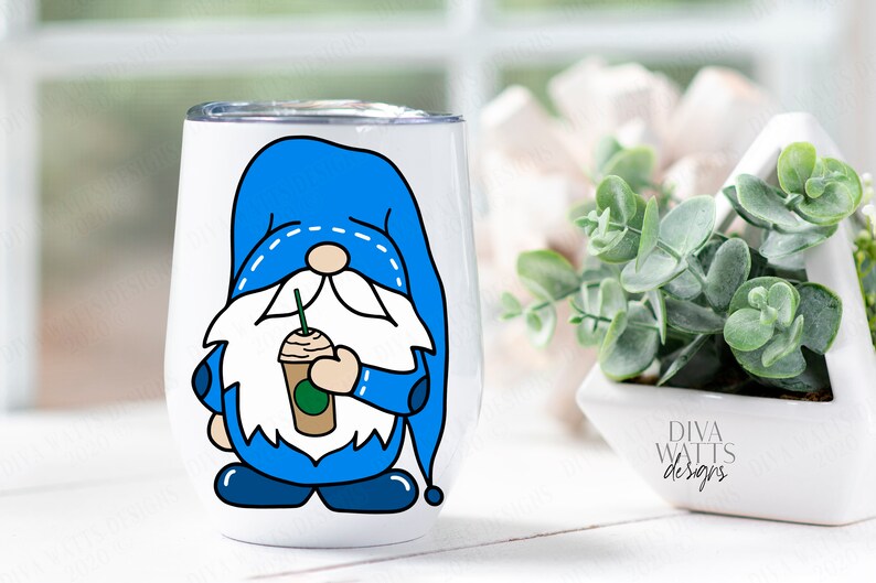 May include: A white stainless steel tumbler with a blue gnome holding a green and brown coffee cup. The gnome has a white beard and a blue hat with white stitching. The tumbler is on a white surface.