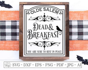 Könnte beinhalten: Ein Holzschild mit dem Text "OLDE SALEM Dead & Breakfast" in Schwarz auf weißem Hintergrund. Eine schwarze Krähensilhouette befindet sich auf der rechten Seite. Dekoriert mit Halloween-Elementen, darunter Fledermäuse und Spinnweben.