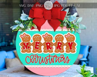 以下が含まれることがあります： 赤い文字で「MERRY」と書かれた、ジンジャーブレッドマンが手をつないでいる丸いクリスマスデコレーション。「Christmas」の文字が下に筆記体で書かれています。赤いリボンと緑で飾られています。