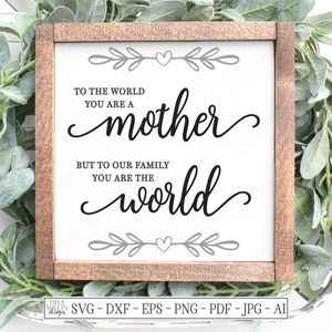 May include: A white sign with a wood frame and a black cursive inscription that reads "To the world you are a mother, but to our family you are the world". The sign is decorated with a gray heart and leaves.