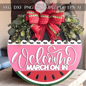 May include: A round wooden door hanger shaped like a watermelon with a red and green watermelon design. The door hanger has a pink welcome sign with the text "Welcome March On In" in white. The door hanger is decorated with a red bow and green leaves.