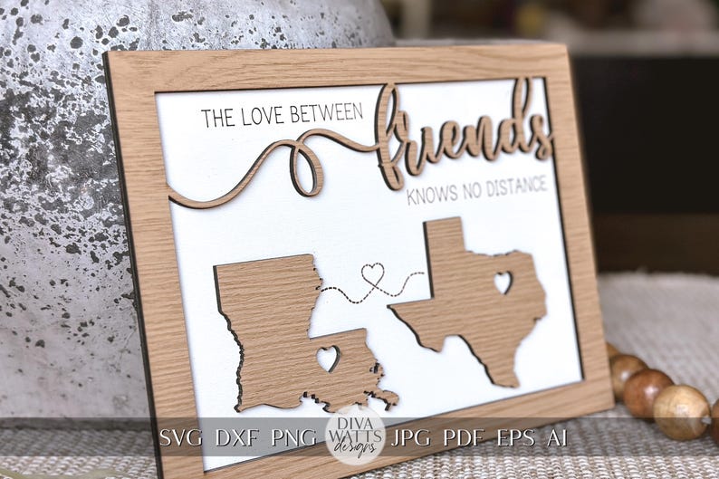 May include: A wooden sign with the text "The love between friends knows no distance" and two state outlines of Louisiana and Texas with hearts in the middle. The sign is on a brown surface.