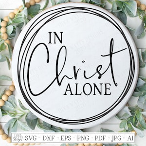 May include: A white round wooden sign with black text that reads "IN Christ ALONE" surrounded by a wreath of green leaves and beige beads.