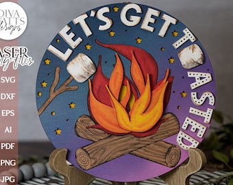 Könnte beinhalten: Ein rundes Holzschild mit dem Text "Let's Get Toasted" in weißen Buchstaben. Das Schild zeigt ein Lagerfeuer mit orangefarbenen und roten Flammen, zwei Holzscheiten und eine Marshmallow auf einem Stock. Der Hintergrund ist dunkelblau mit weißen Sternen.