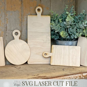 May include: Five unfinished wooden cutting boards of various shapes and sizes, including a rectangle, a circle, and a square. The boards are arranged on a wooden shelf with a potted plant in the background. The text "SVG LASER CUT FILE" is visible at the bottom of the image.