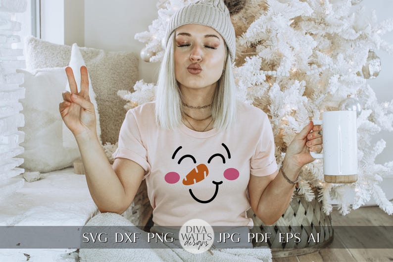 Peut inclure: Une femme portant un t-shirt rose avec un motif de visage de bonhomme de neige souriant. Le bonhomme de neige a des joues roses et un nez de carotte. La femme tient une tasse blanche avec une poign&eacute;e en bois.