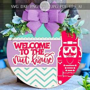 May include: A round wooden sign with a purple and teal background, featuring the text "WELCOME TO THE nut house" in red. A red nutcracker figure is on the right. The sign is decorated with a purple bow and greenery.