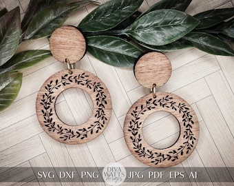 May include: A pair of wooden earrings with a circular design featuring a wreath of leaves. The earrings are brown and have a natural wood finish.