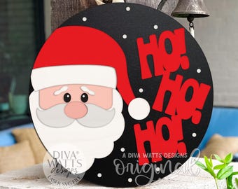 May include: A round, black Christmas sign featuring Santa Claus and the words "HO! HO! HO!" in red. Santa has a red hat, white beard, and a pink nose. The sign includes the text "A Diva Watts Designs original".