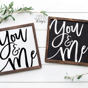 May include: Two wooden signs with the text "You & Me" written in black and white calligraphy. The signs are on a white wood background.